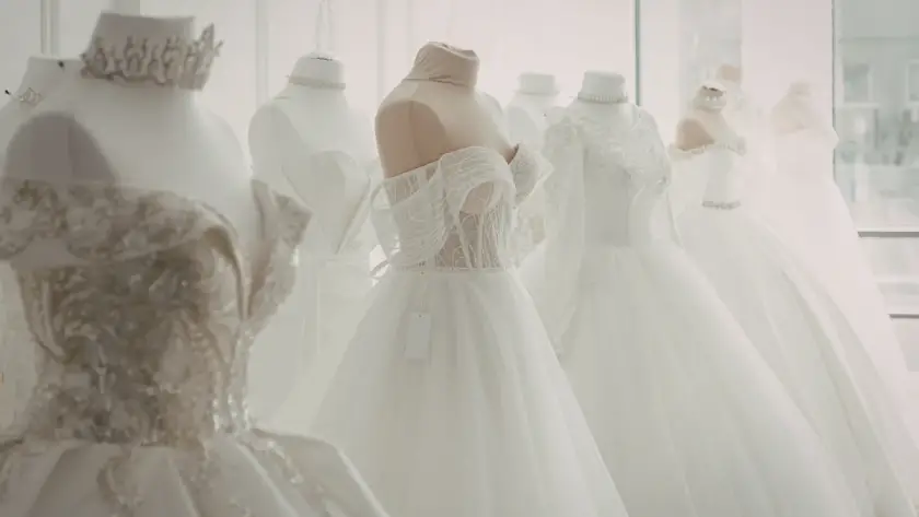 Bridal boutique display of elegant white wedding dresses on mannequins, featuring lace details, off-the-shoulder styles, and full tulle skirts in a bright showroom