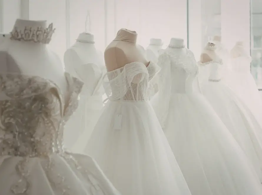 Bridal boutique display of elegant white wedding dresses on mannequins, featuring lace details, off-the-shoulder styles, and full tulle skirts in a bright showroom