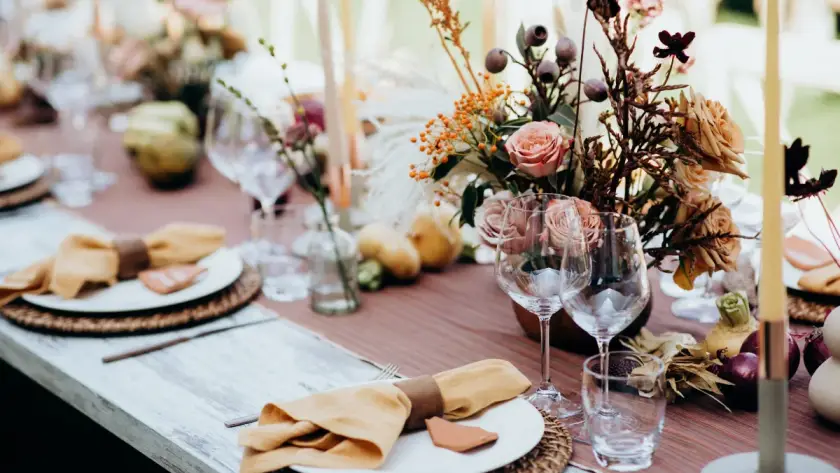 Spring wedding table setting with blush roses, earthy florals, amber napkins, candles, and elegant glassware on a rustic outdoor reception table