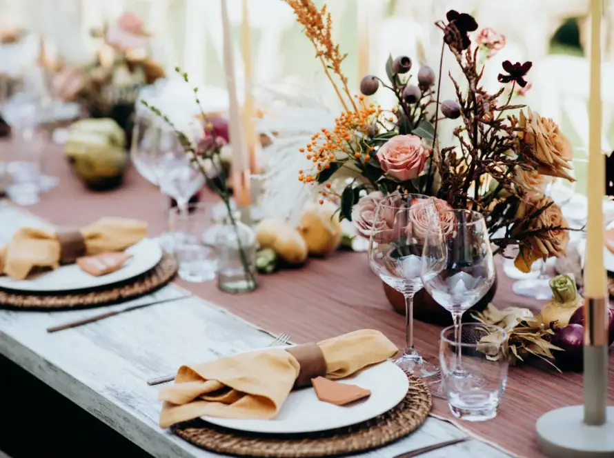 Spring wedding table setting with blush roses, earthy florals, amber napkins, candles, and elegant glassware on a rustic outdoor reception table