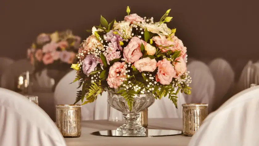 Elegant wedding table centerpiece featuring pink and lavender florals in a glass vase, surrounded by votive candles on a softly lit reception table