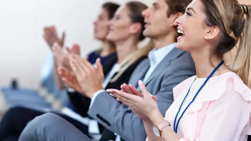 Attendees applauding at a corporate conference, smiling and engaged during a business presentation or seminar