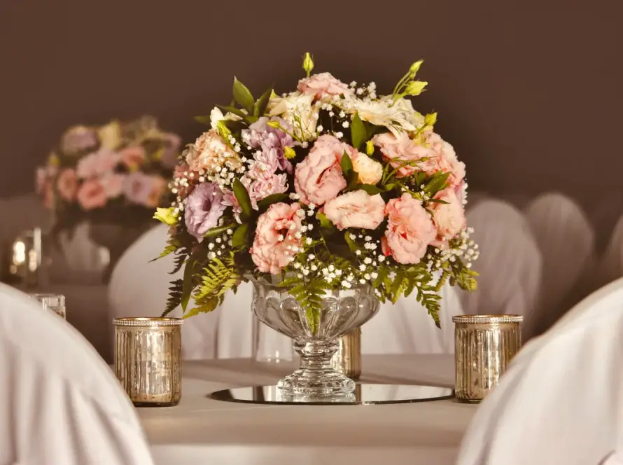 Elegant wedding table centerpiece featuring pink and lavender florals in a glass vase, surrounded by votive candles on a softly lit reception table