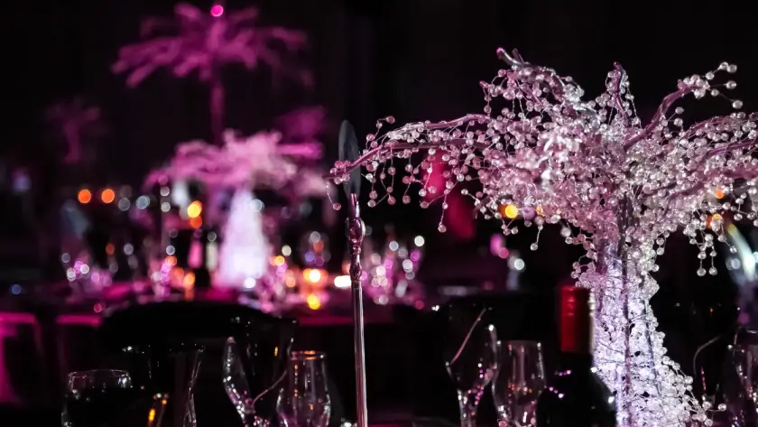 Elegant gala table setting with crystal-like decorative centerpieces, soft candlelight, and pink ambient lighting creating a luxurious event atmosphere
