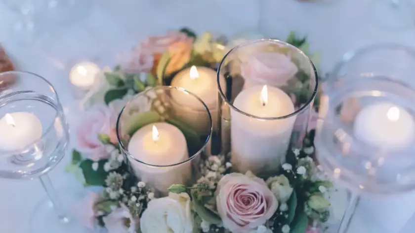 Romantic wedding table centerpiece with floating candles in glass cylinders surrounded by soft pink roses and greenery on an elegant reception table