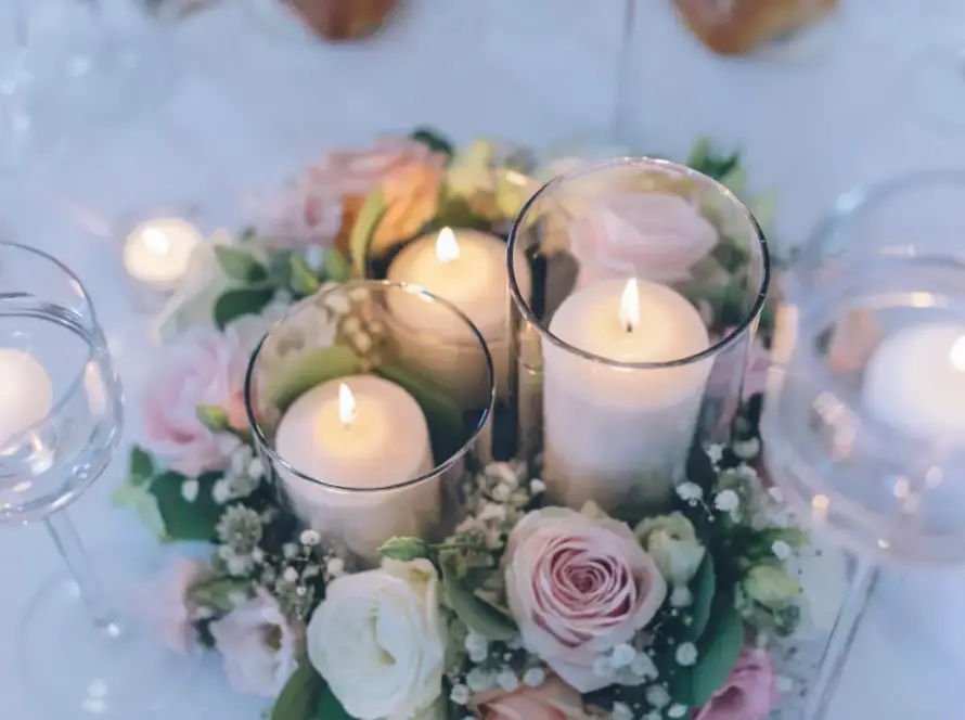 Romantic wedding table centerpiece with floating candles in glass cylinders surrounded by soft pink roses and greenery on an elegant reception table