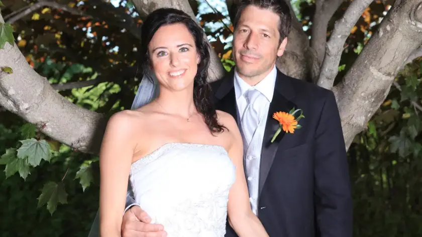 Bride and groom posing together outdoors by a tree, smiling in formal wedding attire during a romantic portrait