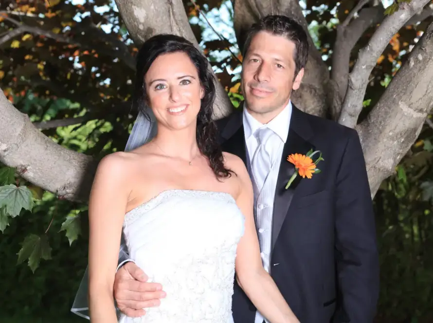 Bride and groom posing together outdoors by a tree, smiling in formal wedding attire during a romantic portrait